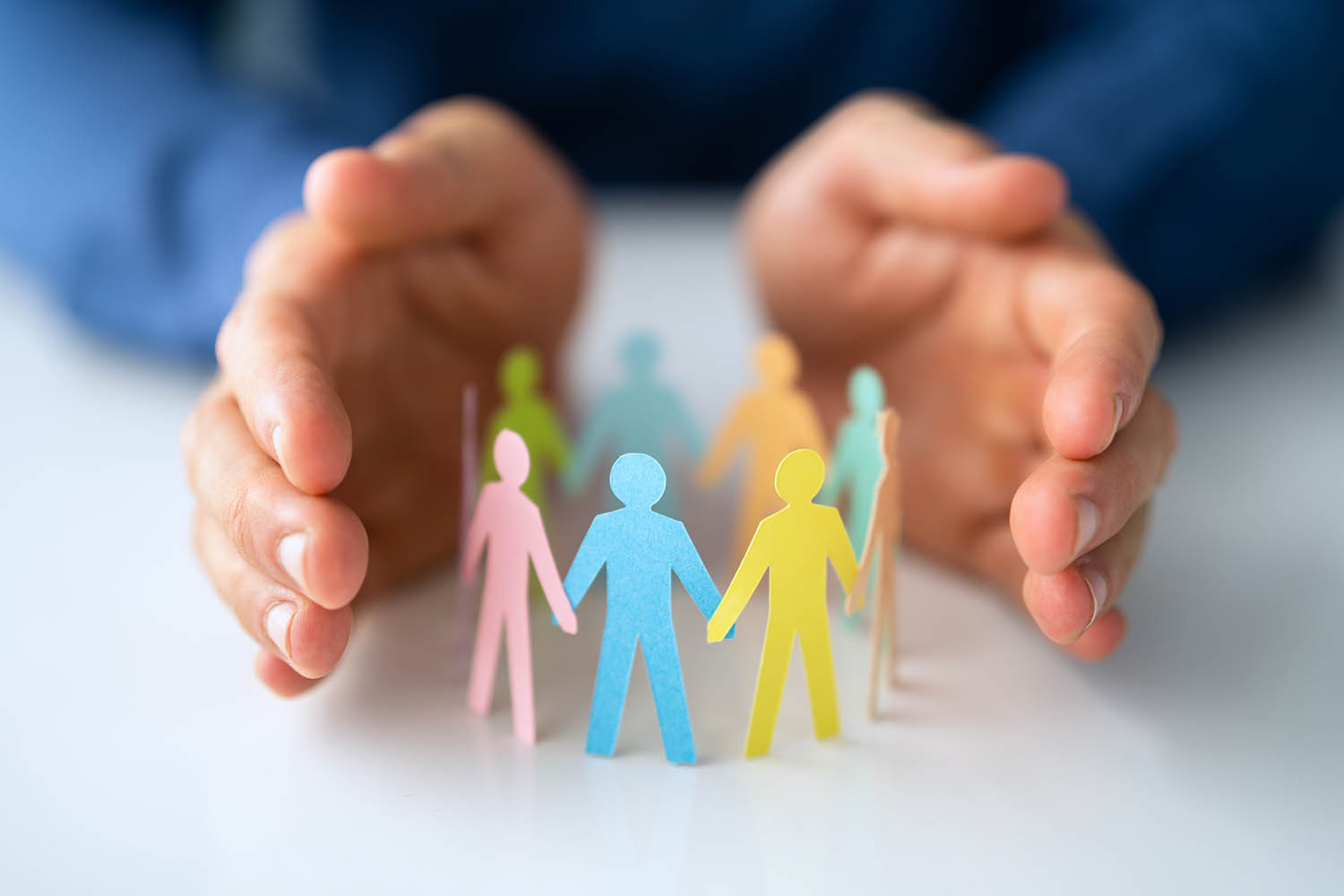 a photograph of two hands encircling some paper figures - to represent adult safeguarding